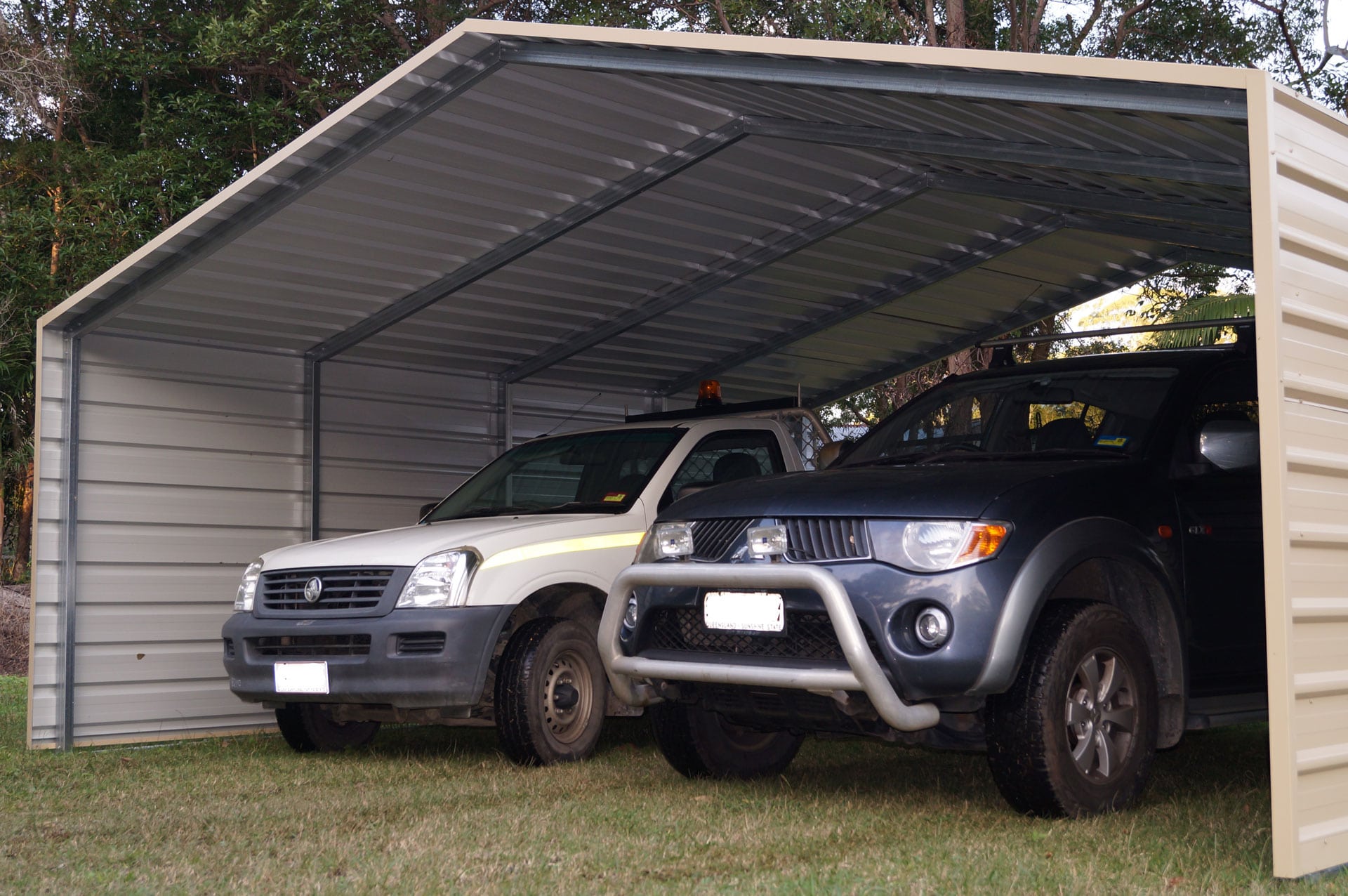 Two utes parked under a car shelter.