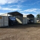Shade sheds with parked caravan and cars inside next to shipping containers